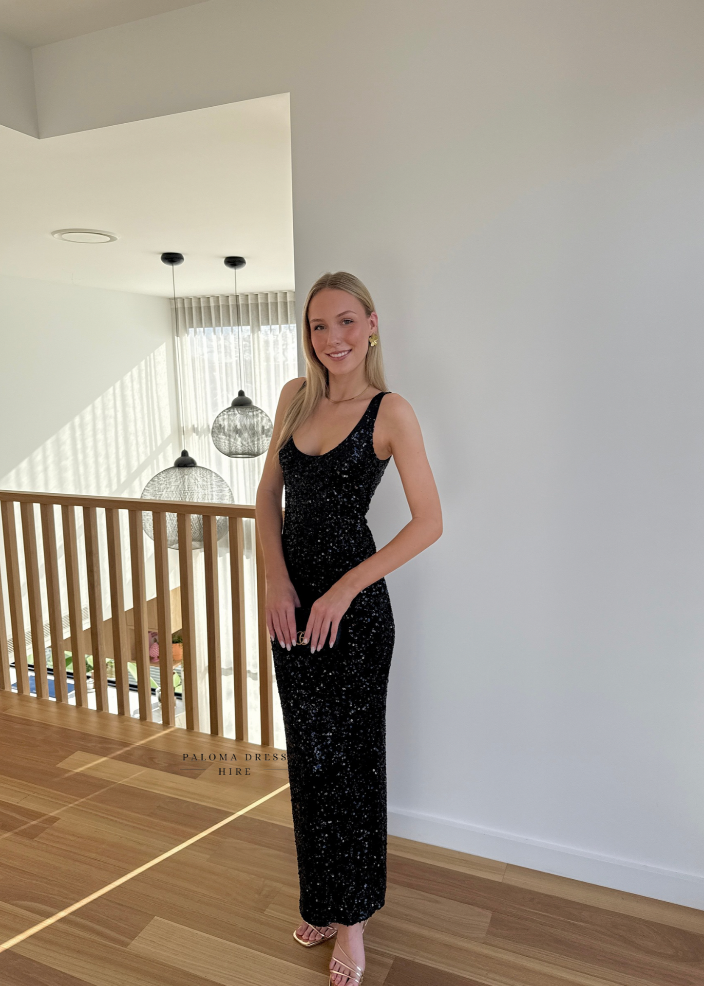 Woman in a black sequin dress standing in a modern indoor setting.