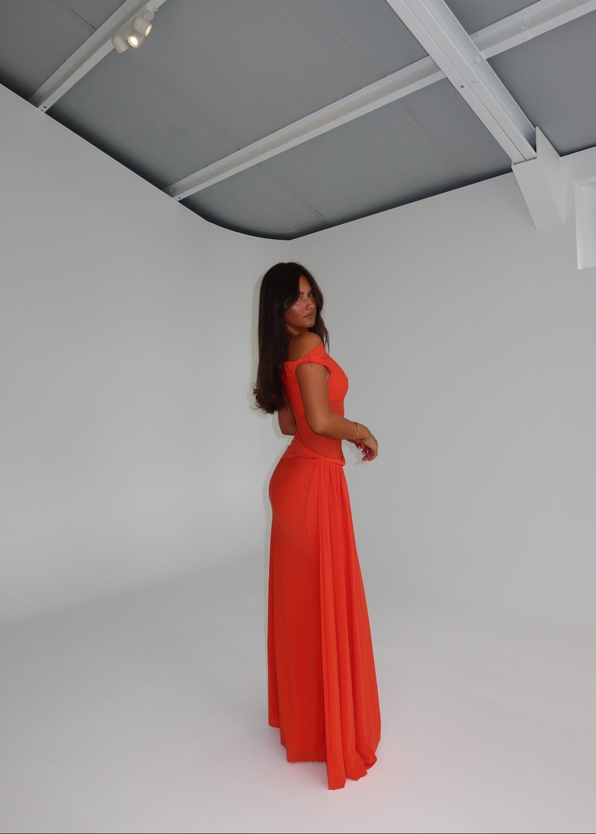 Woman in a bright orange dress standing against a white background
