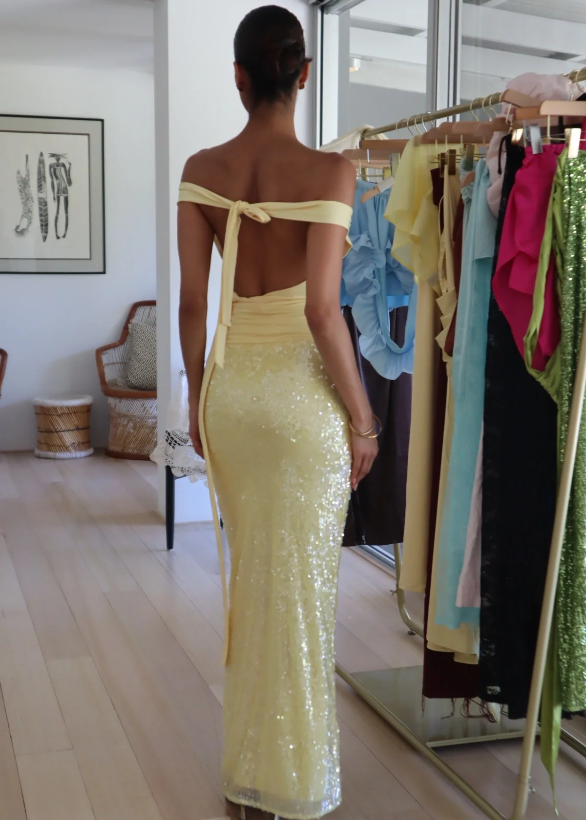 Woman in a yellow sequin dress standing in front of a rack of clothes.