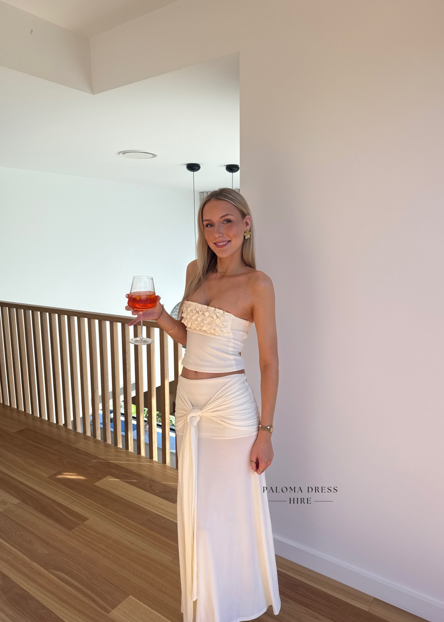 Woman in a white strapless dress holding a drink indoors.