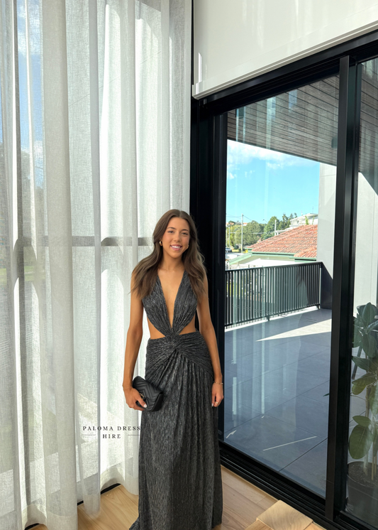 Woman in a gray dress standing in a modern interior setting with large windows.