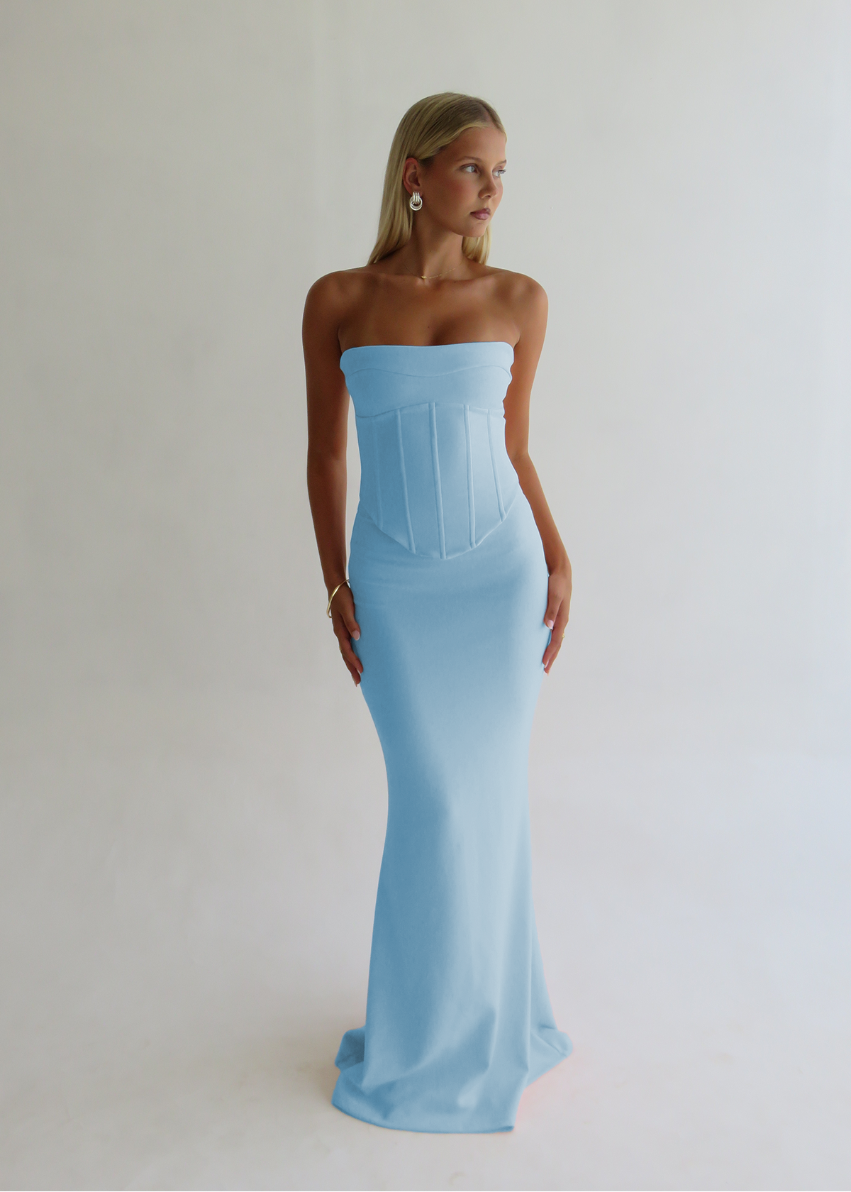 Woman wearing a light blue strapless gown against a plain background
