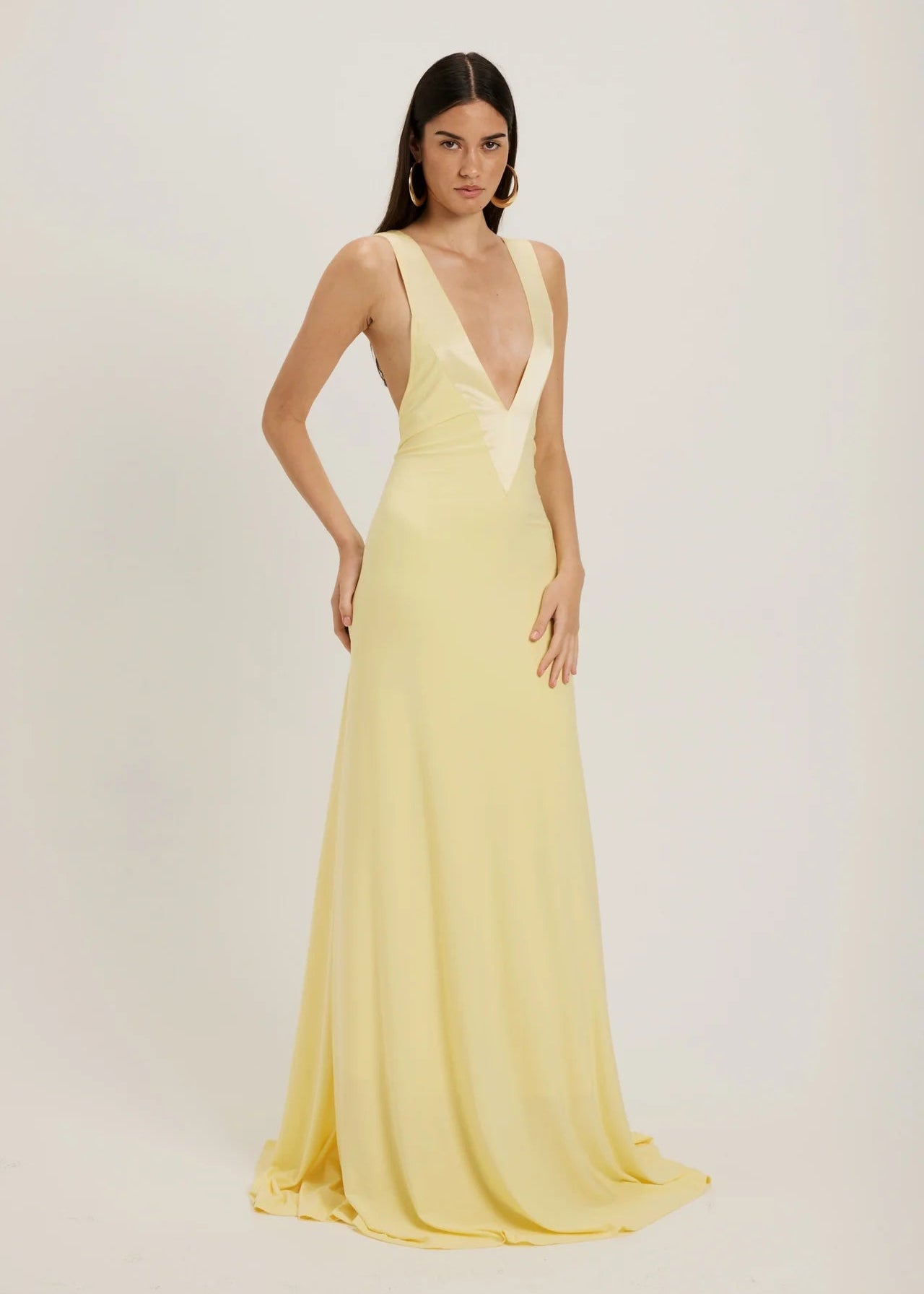 Woman wearing a light yellow evening gown with a plunging neckline on a plain background