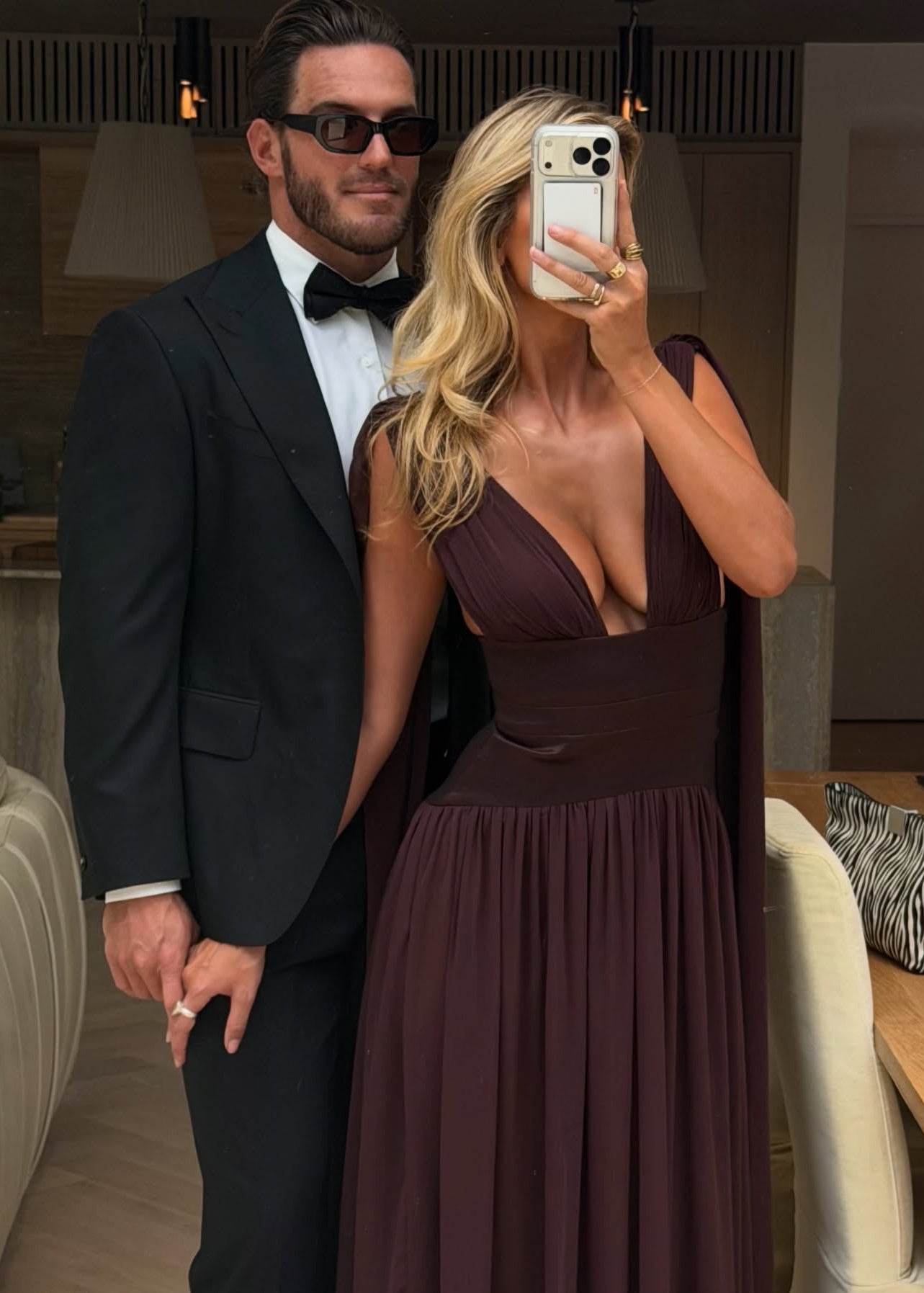Man in a tuxedo and woman in a deep neckline dress taking a selfie.