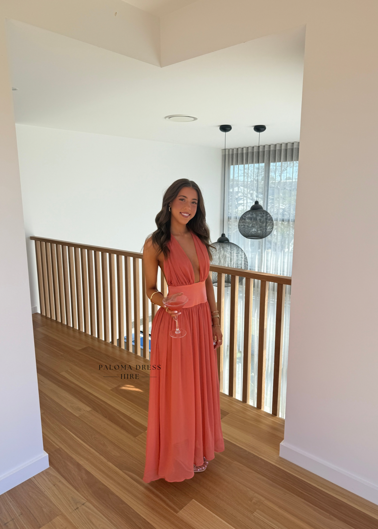 Woman in a long coral dress standing in a modern interior setting.