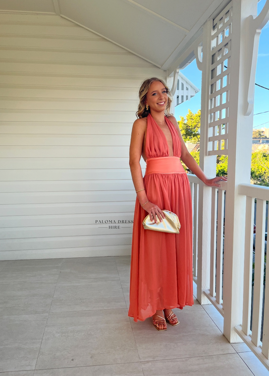 Woman in a coral dress standing on a porch with a blurred background