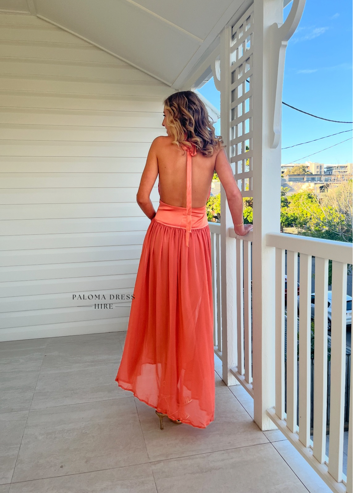 Woman in a coral dress standing on a balcony with a scenic view.