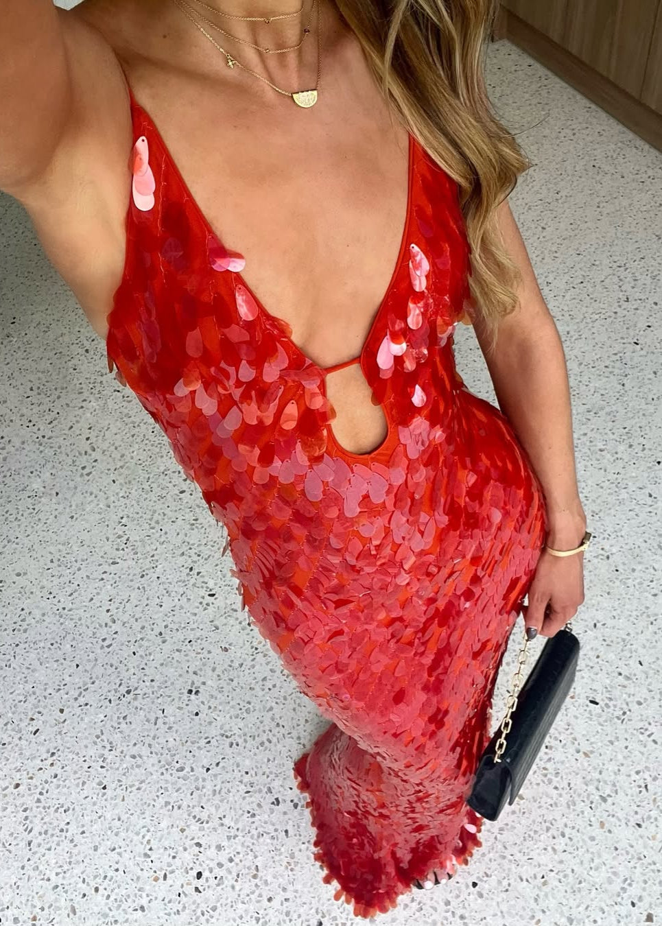 Person wearing a red sequin dress with a deep neckline on a light gray floor.
