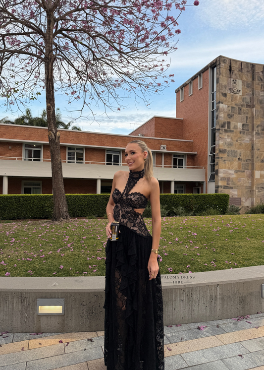 Woman in a black lace dress standing in front of a brick building with cherry blossoms.