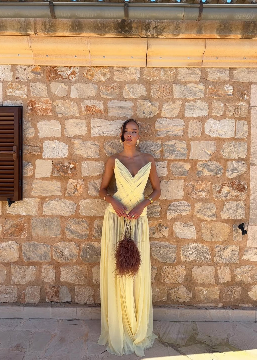Woman in a yellow dress standing against a stone wall.