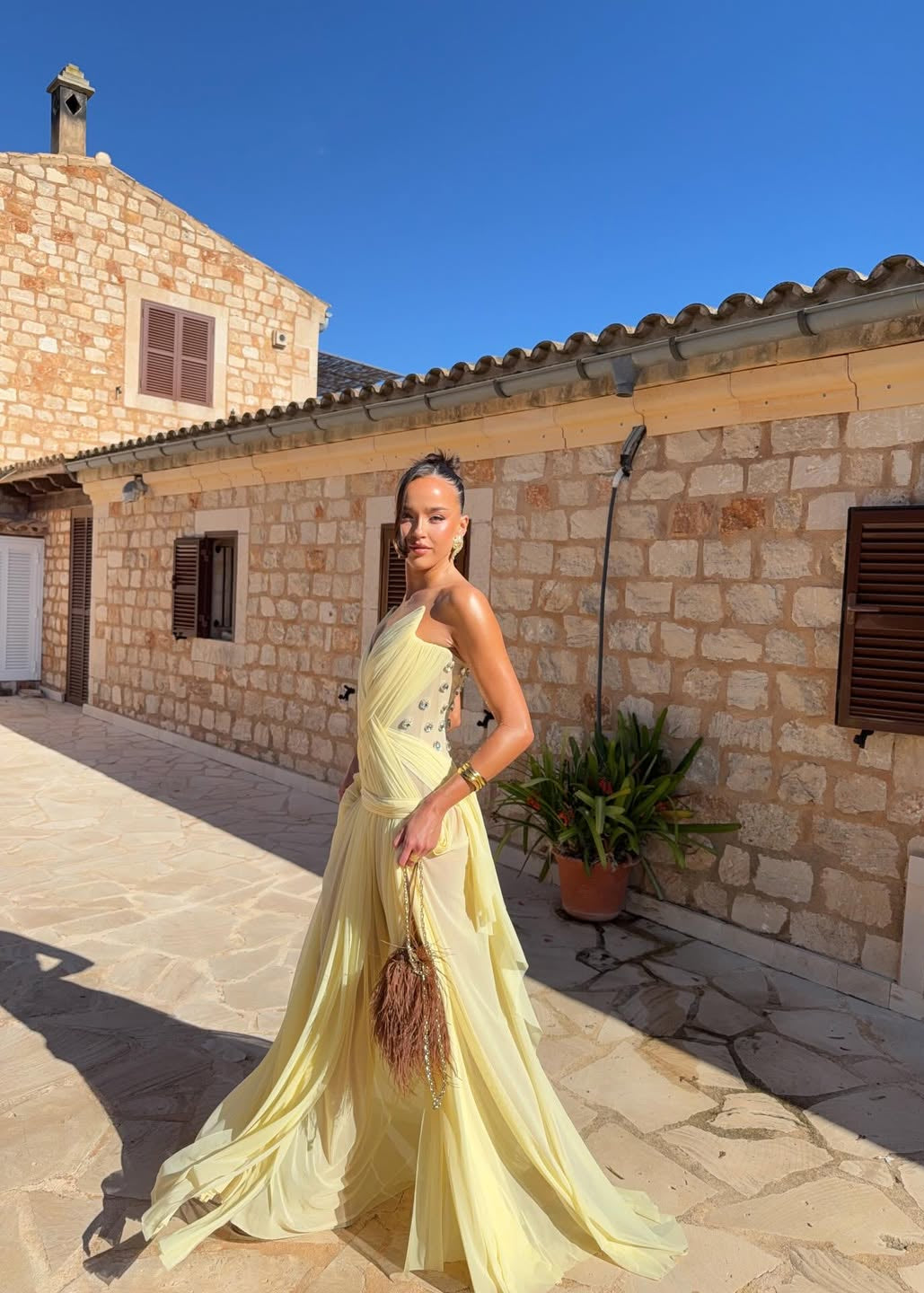 Woman in a yellow dress standing in front of a stone building with a clear blue sky.