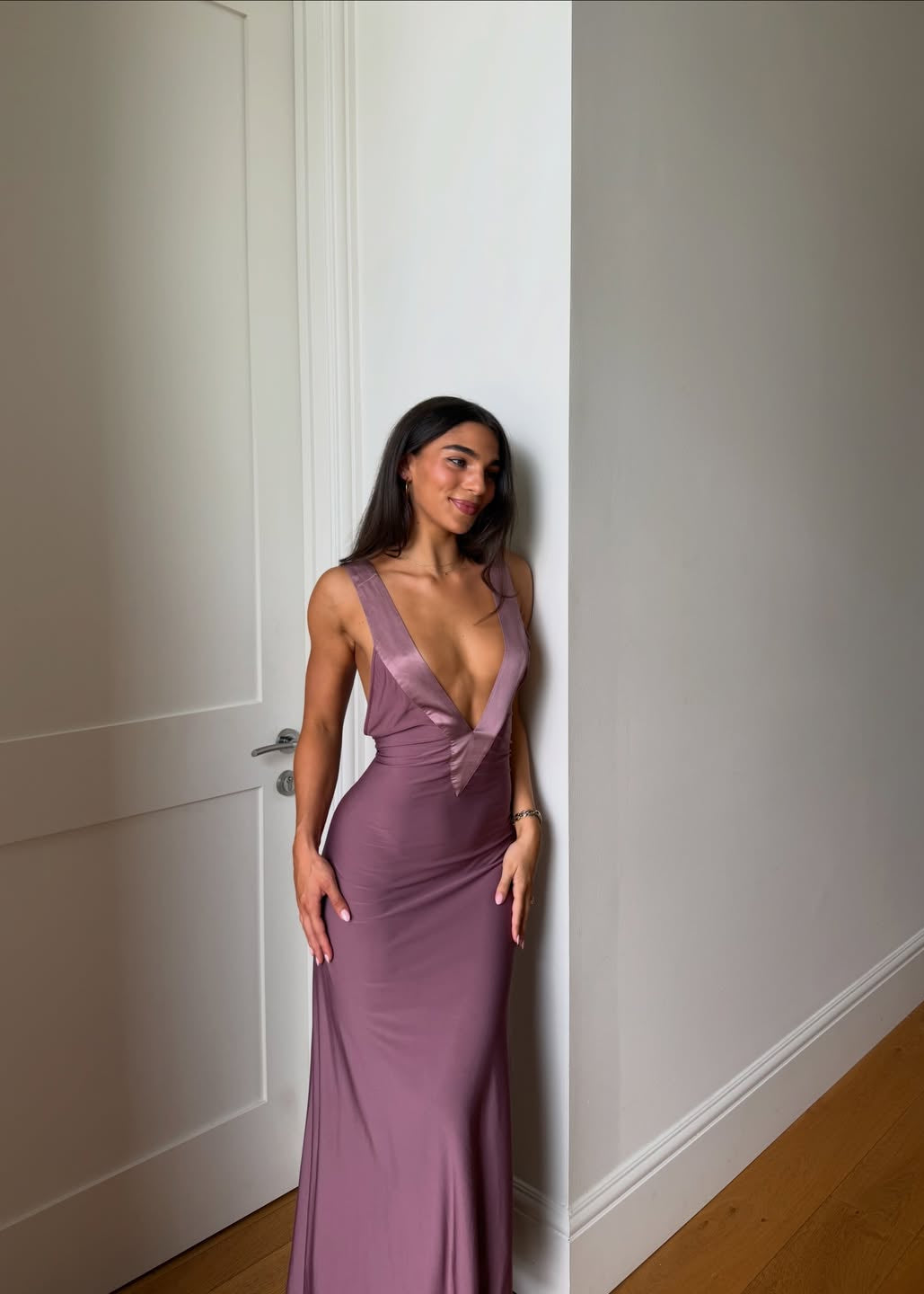 Woman in a purple gown standing against a white wall.