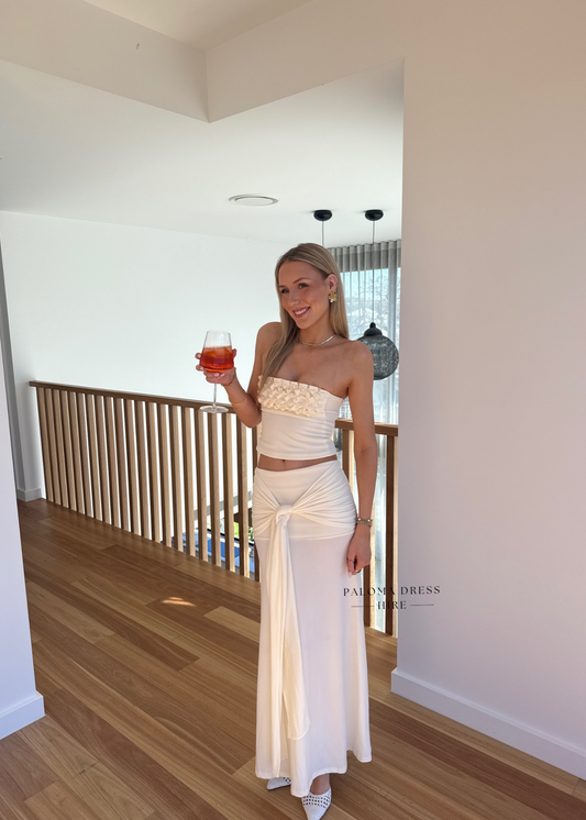 Woman in a white strapless dress holding a glass of red wine indoors.